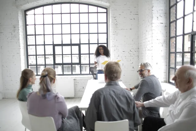 Diverse group discussing ideas in a bright conference room with large windows and a white brick interior. Likviditetsstyring for SMV'er: budget, likviditetsprognose og kreditorfrister